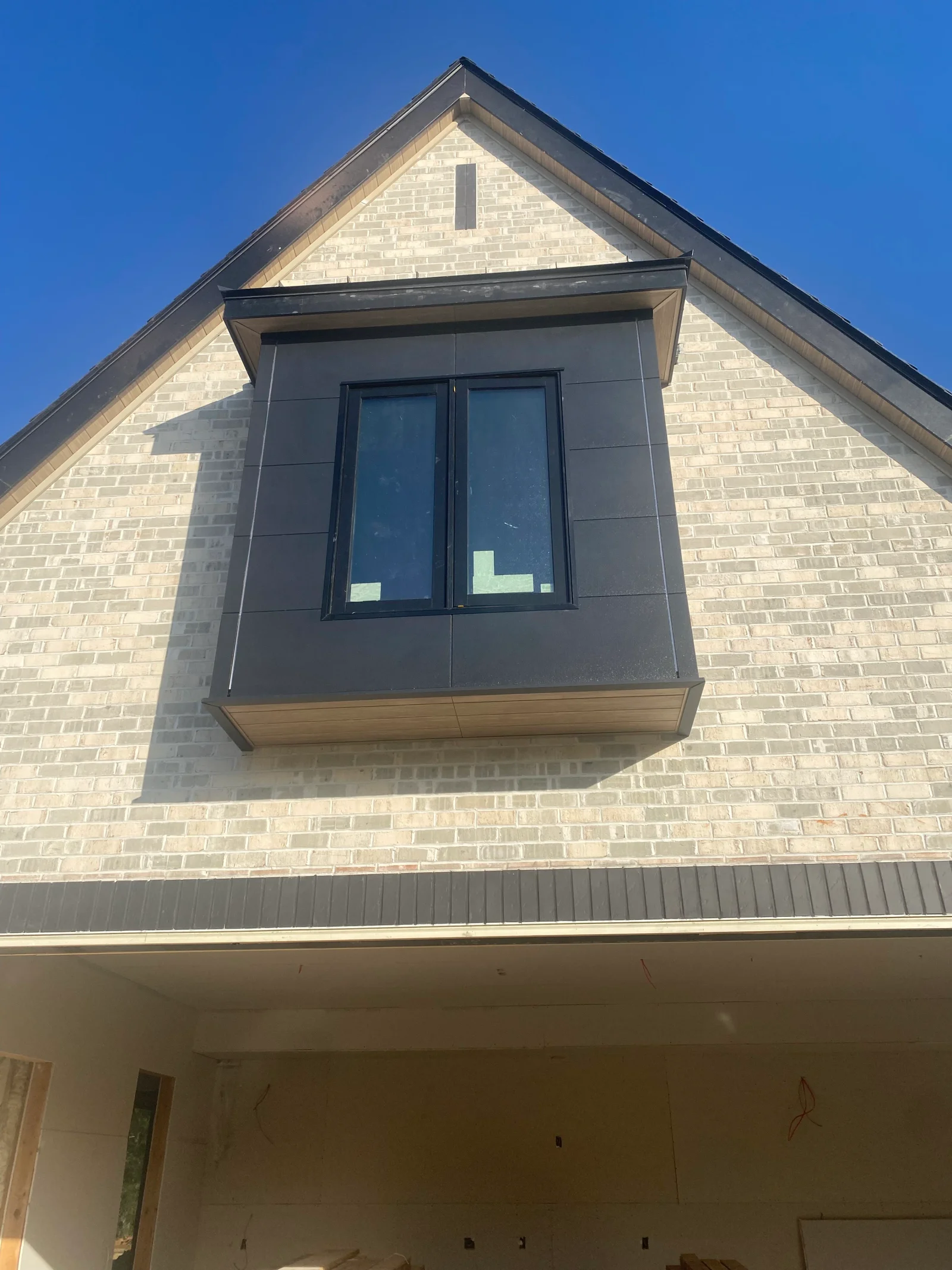 Gable roof addition with dark fascia trim and black window on cream brick home